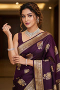 Woman in a purple saree with gold patterns indoors