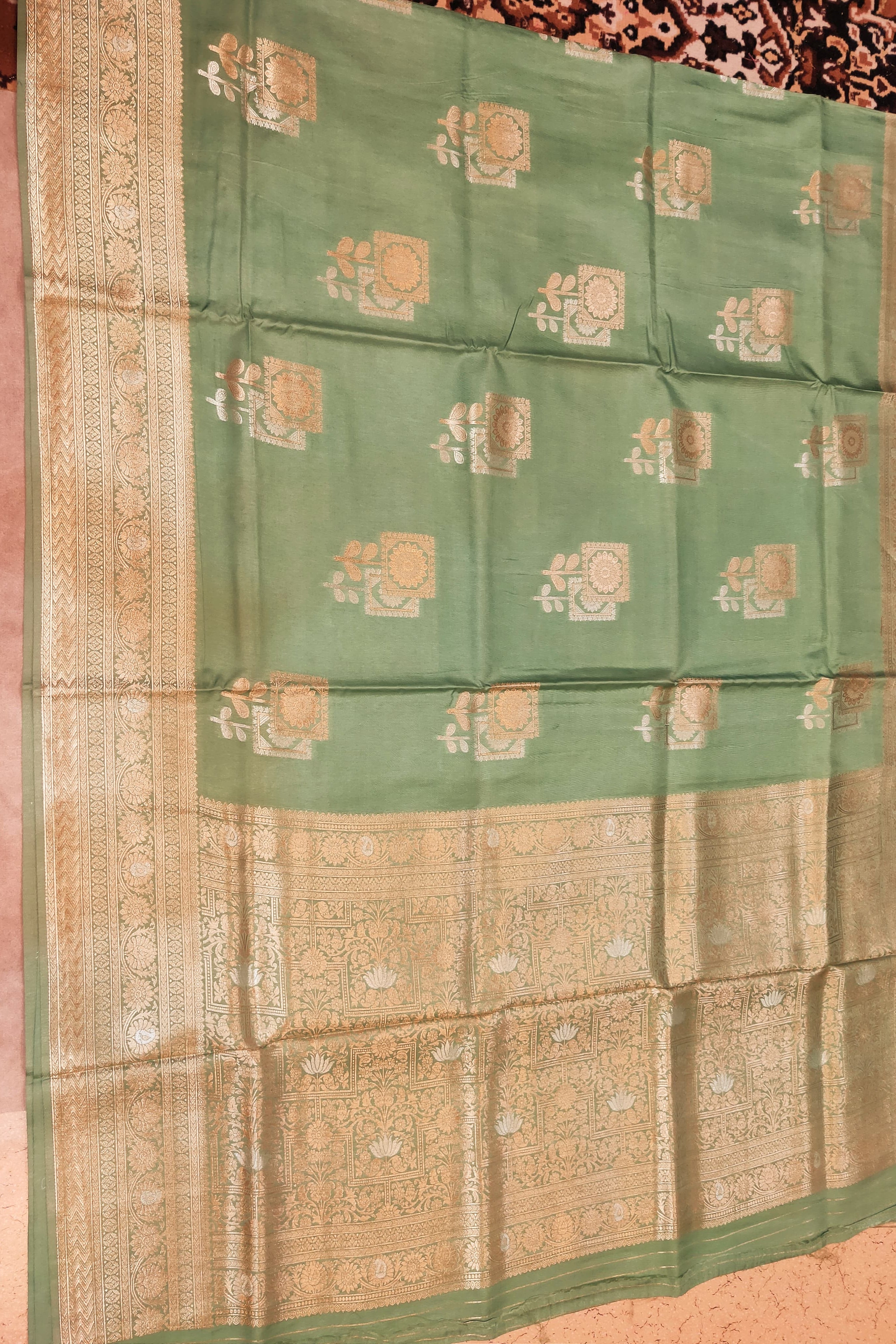 Green and beige saree with floral patterns on a pink background