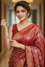 Woman in a red saree with intricate patterns, standing indoors.