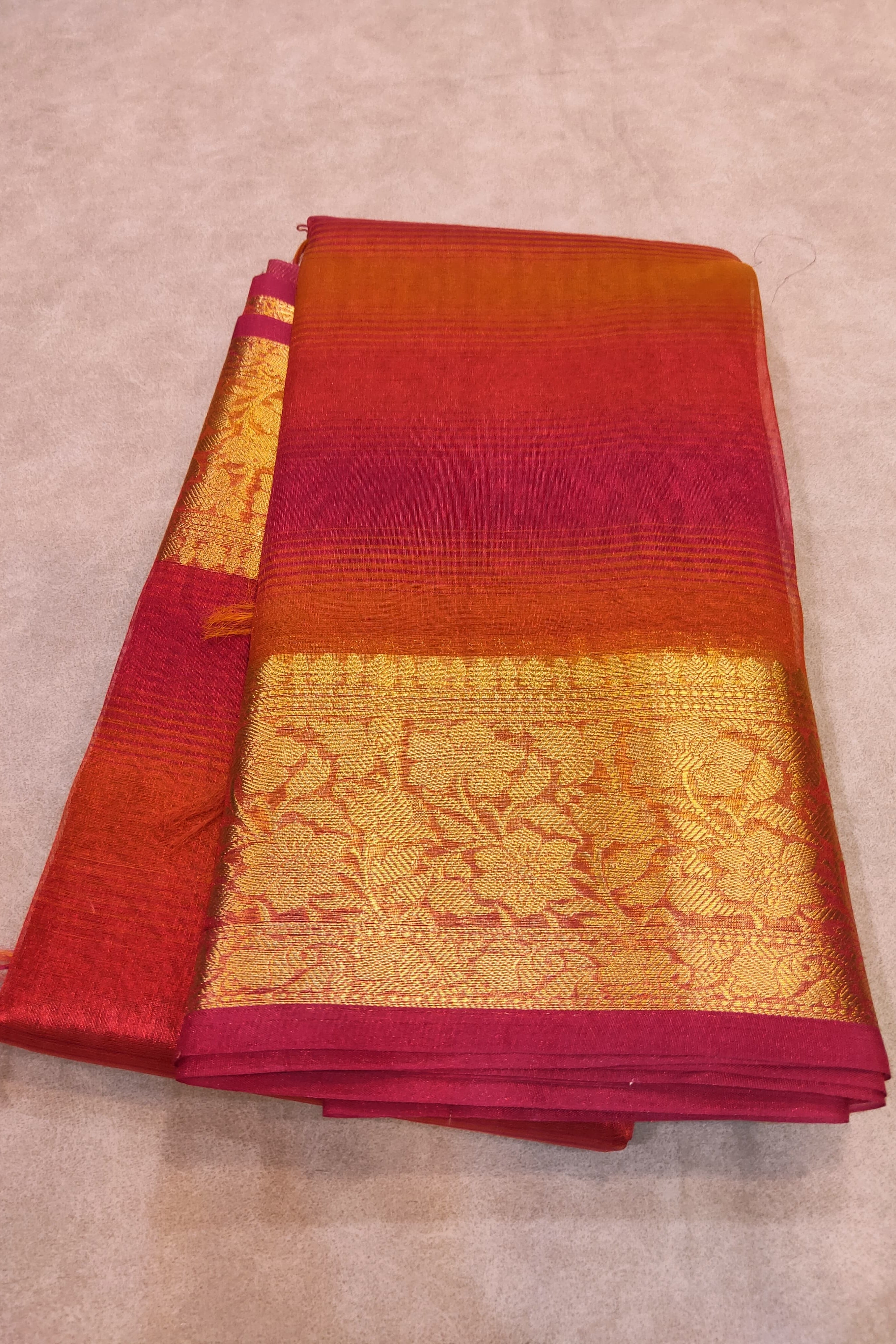 Folded red and gold saree on a beige surface