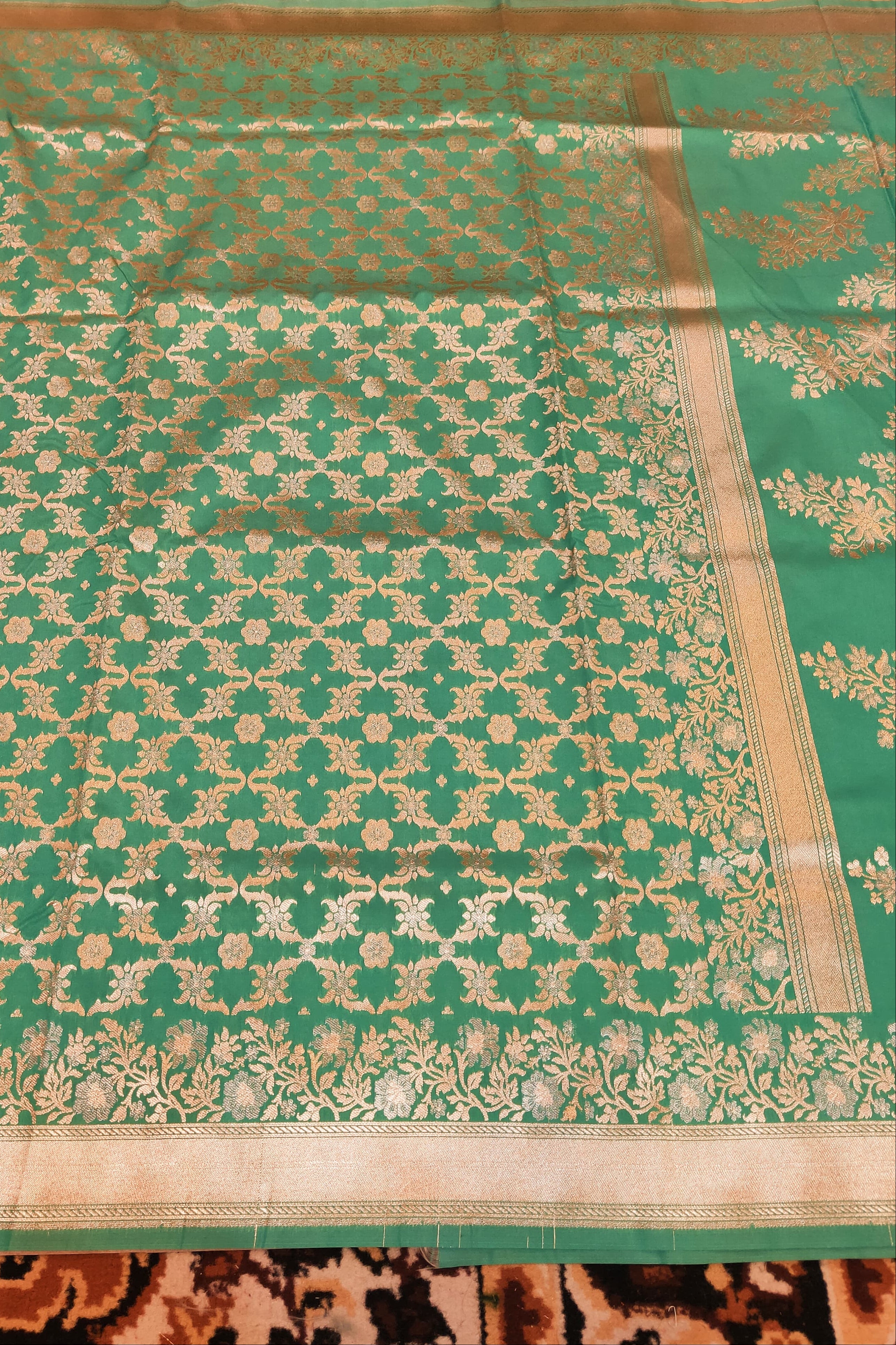 Green saree with gold patterns on a wooden surface