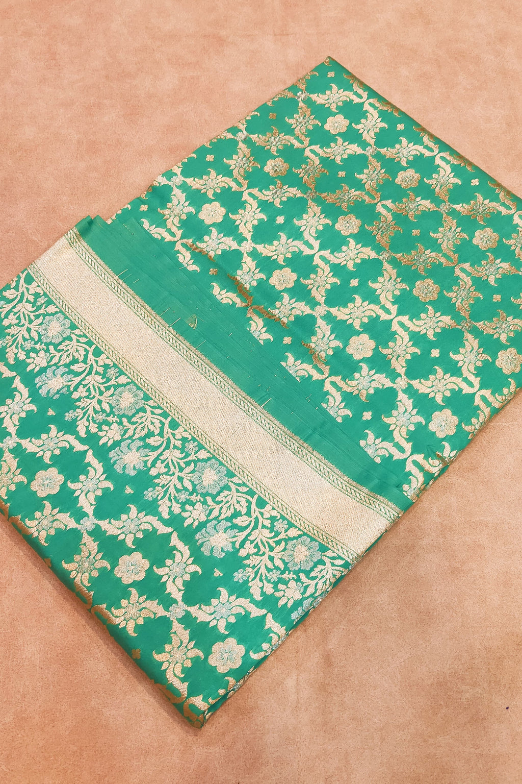 Green saree with gold floral patterns on a beige background