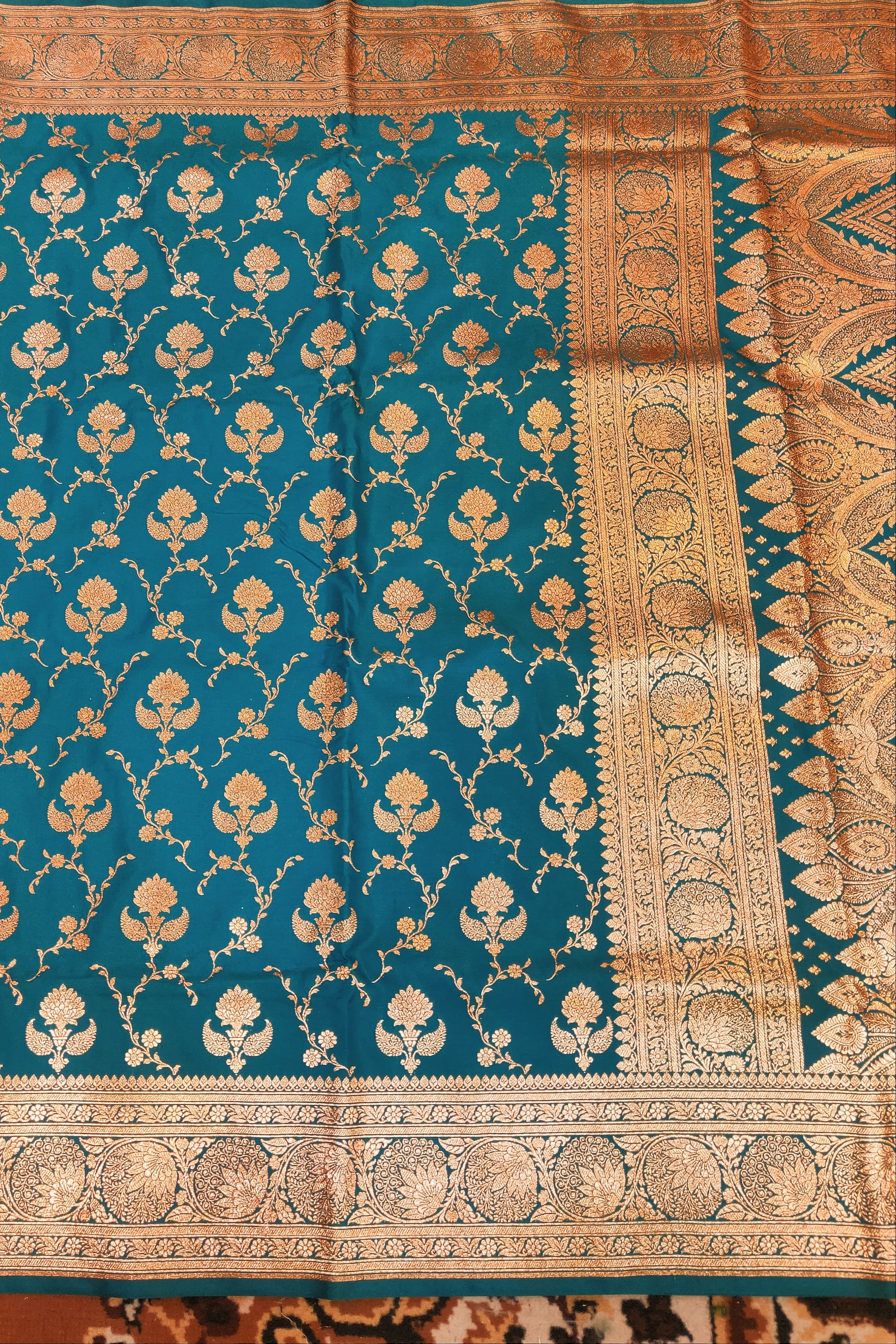 Teal fabric with gold floral patterns on a textured background