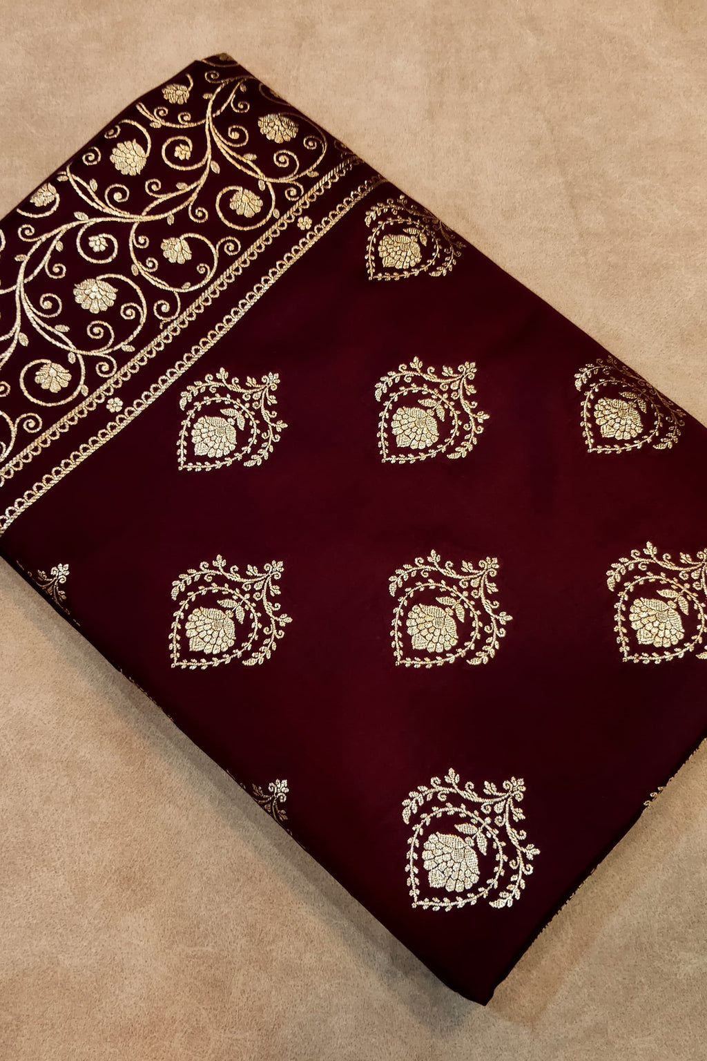 Maroon fabric with gold embroidery on a beige surface