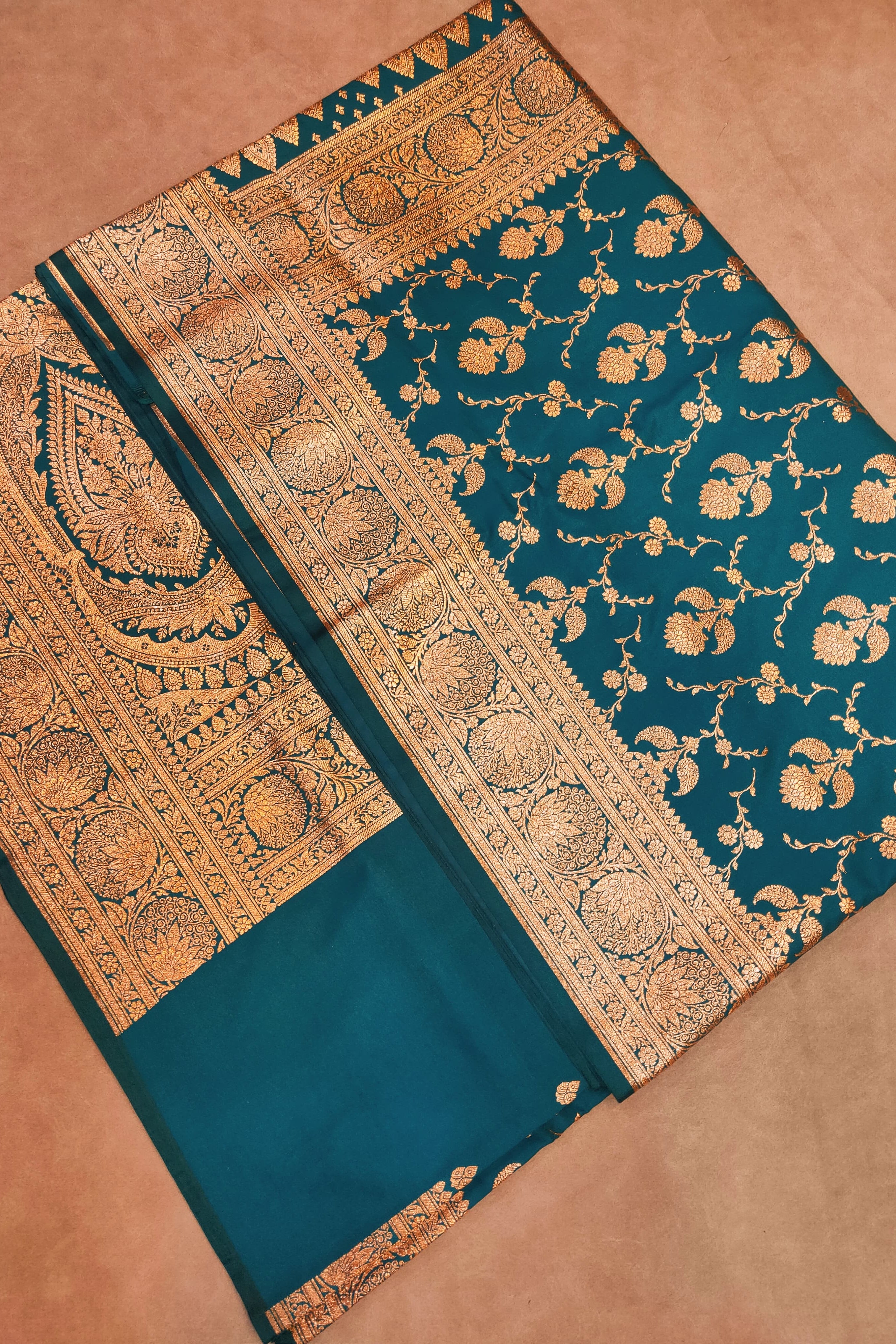 Teal saree with gold intricate patterns on a brown background