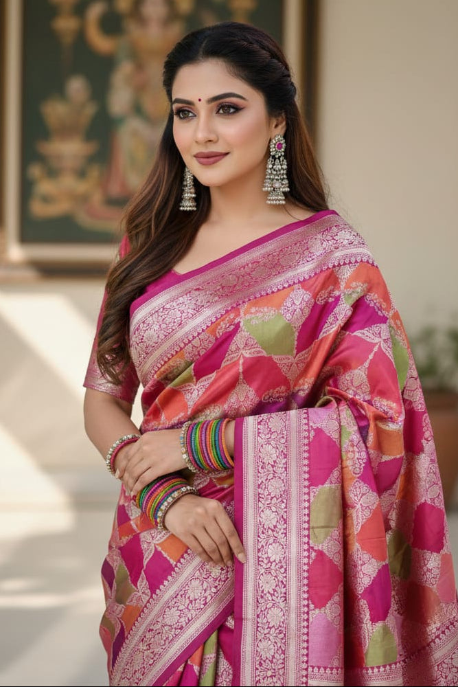 Woman in a colorful saree standing indoors with a decorative painting in the background