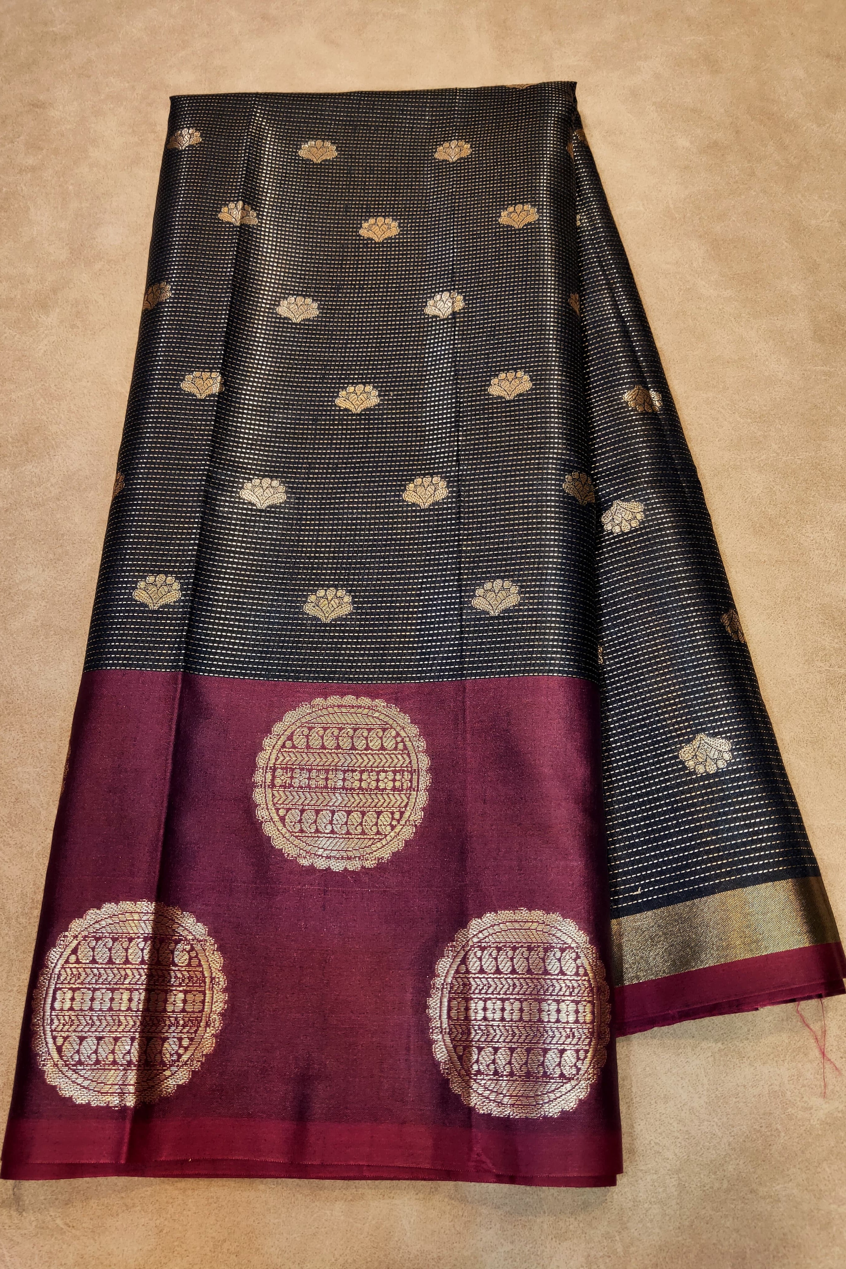 Black and maroon saree with gold patterns on a beige background