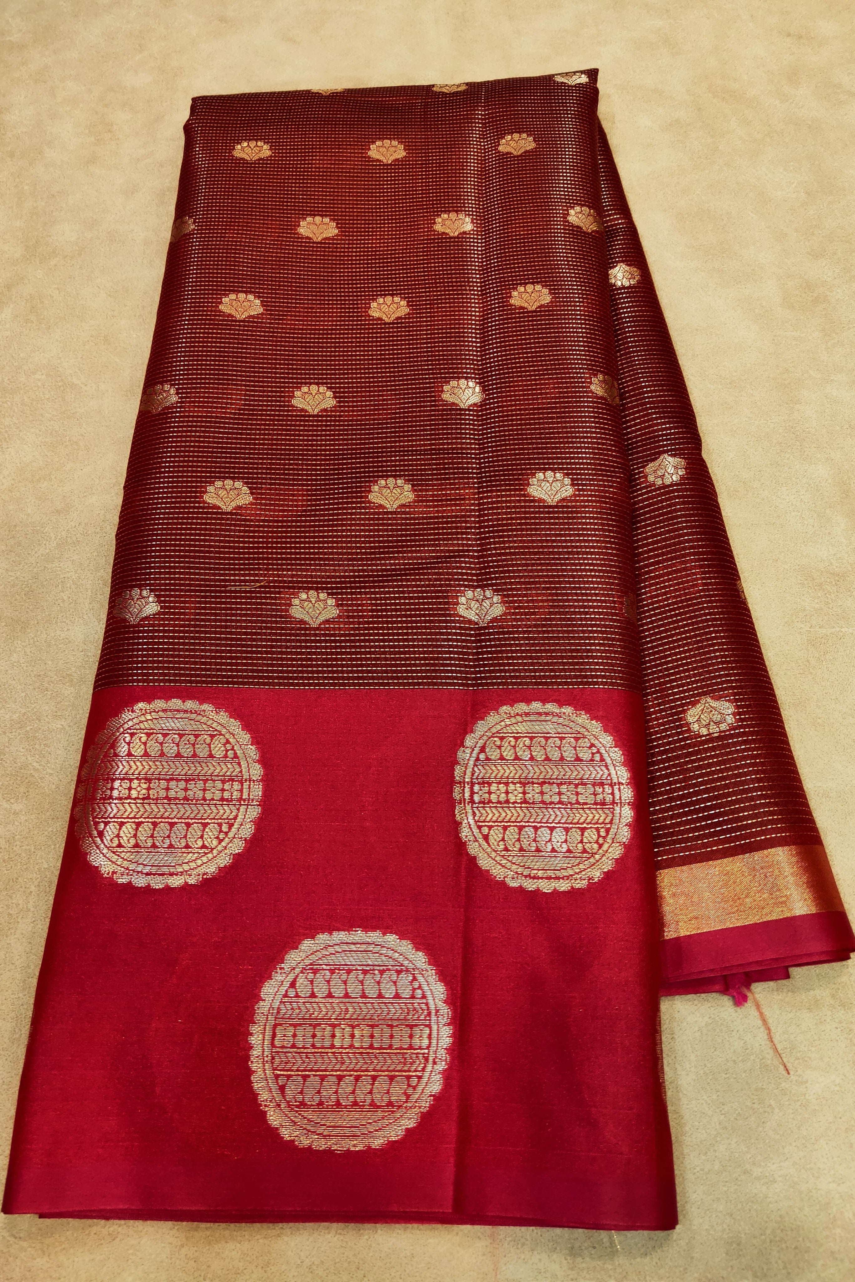 Red and brown saree with gold patterns on a beige background