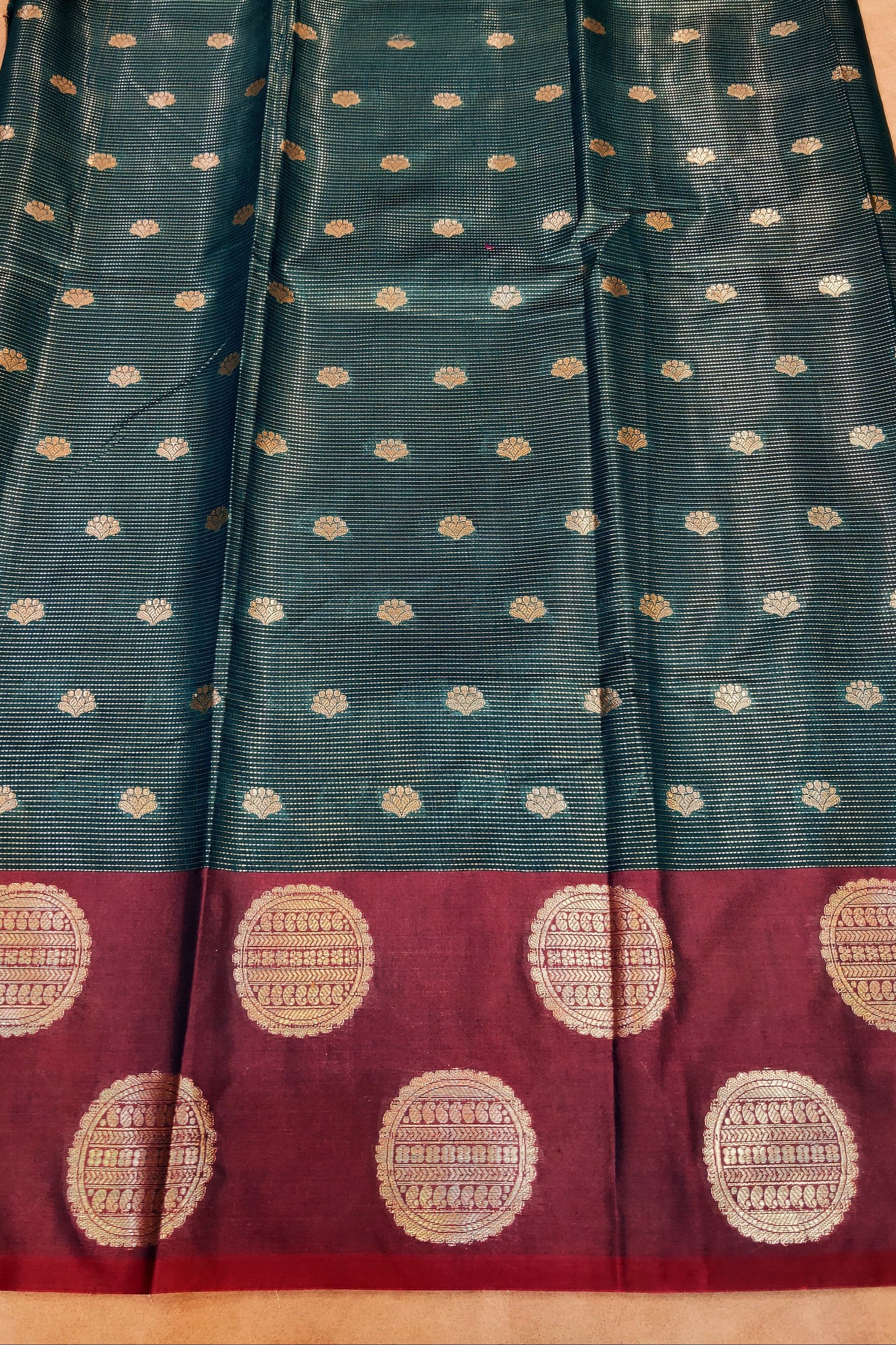 Teal saree with white dot pattern and red border with gold dot pattern on a beige surface.