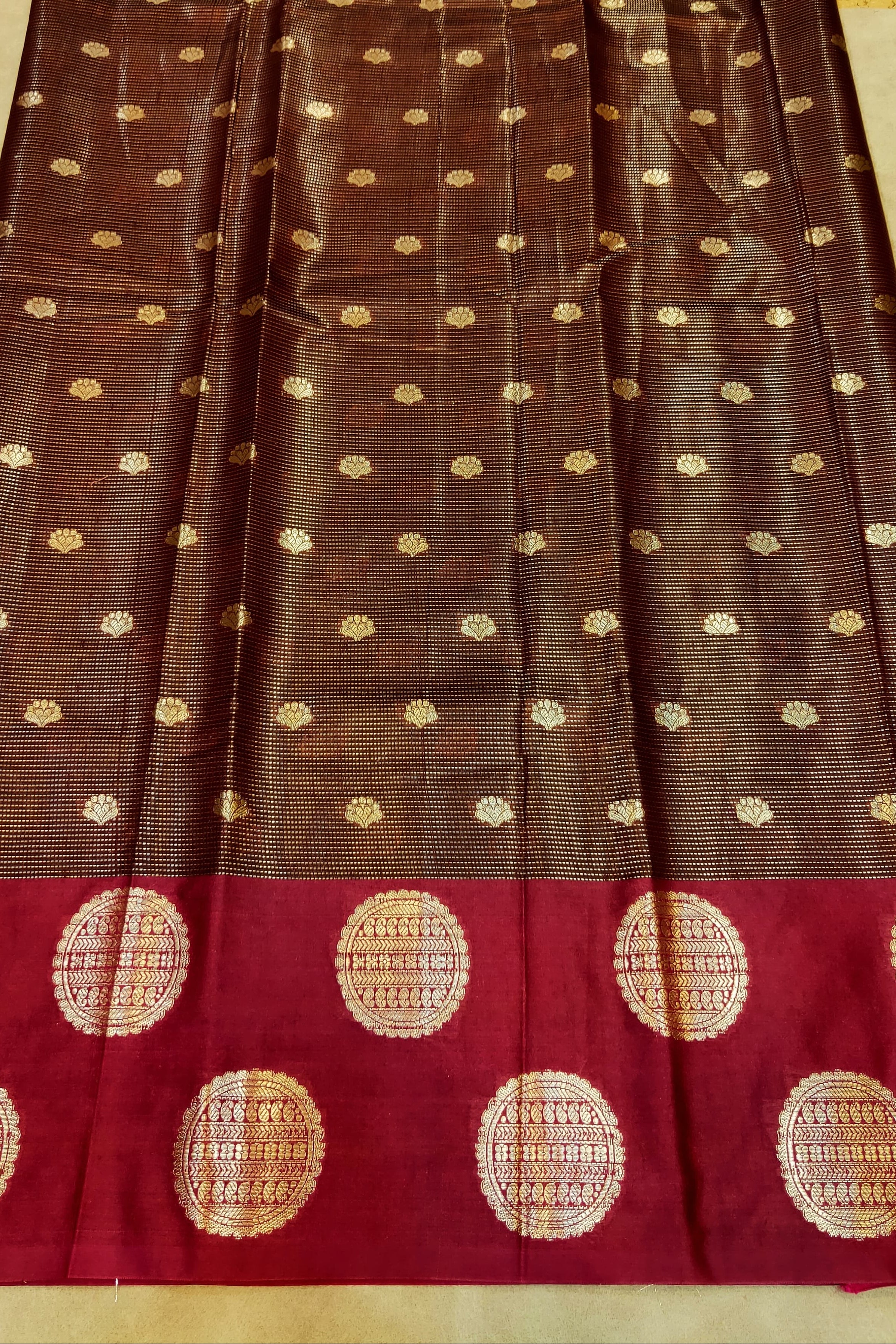 Brown and red saree with gold dot patterns on a beige background