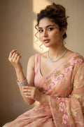 Woman in a pink saree with floral patterns against a neutral background