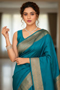 Woman wearing a teal saree with gold border indoors