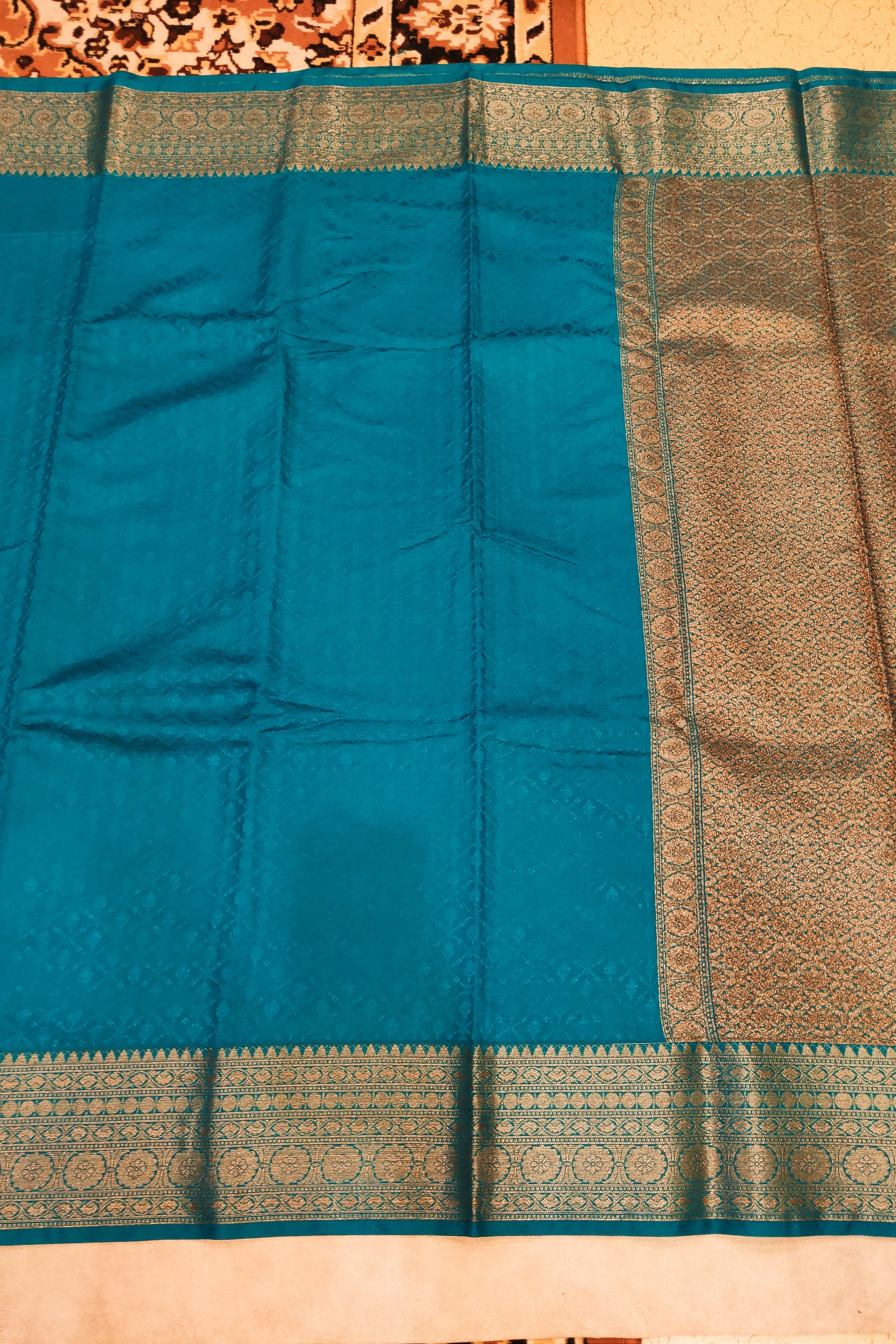 Teal saree with a gold border on a beige background