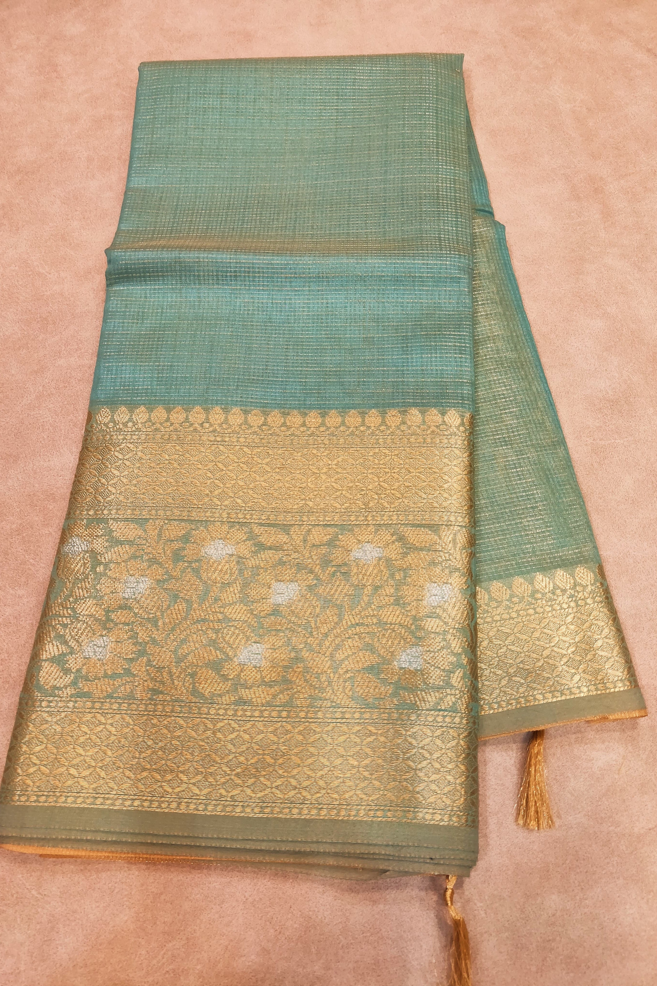 Green and gold saree with intricate patterns on a beige background