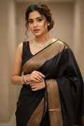 Woman in a black and gold saree with jewelry against a neutral background