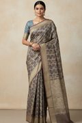 Woman wearing a traditional saree with a beige and brown pattern against a plain background
