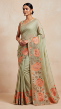 Woman wearing a light green saree with floral patterns on a beige background