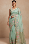 Woman wearing a light green saree with floral patterns on a beige background