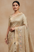 Woman wearing a beige saree with floral embroidery on a beige background