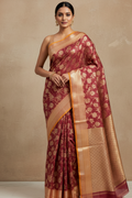 Woman wearing a maroon saree with gold border against a beige background