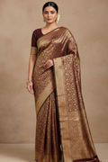 Woman wearing a brown and gold saree against a beige background