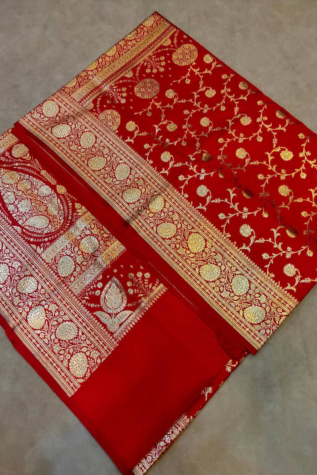 Red fabric with gold and white intricate patterns on a beige background