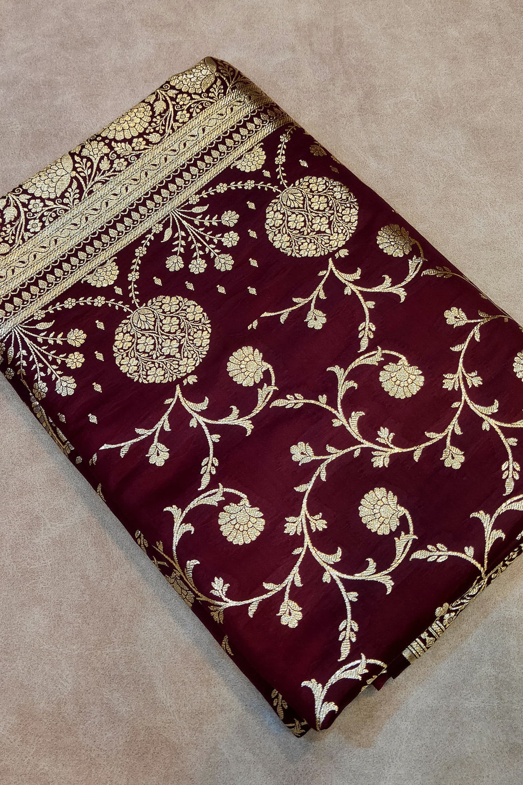 Maroon fabric with gold floral patterns on a beige surface