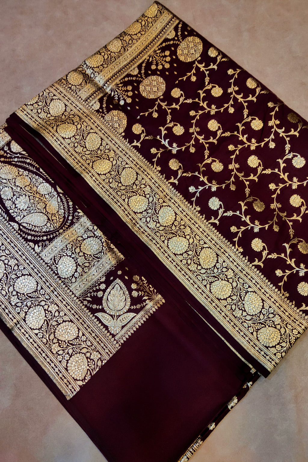 Brown saree with gold and white floral patterns on a beige background