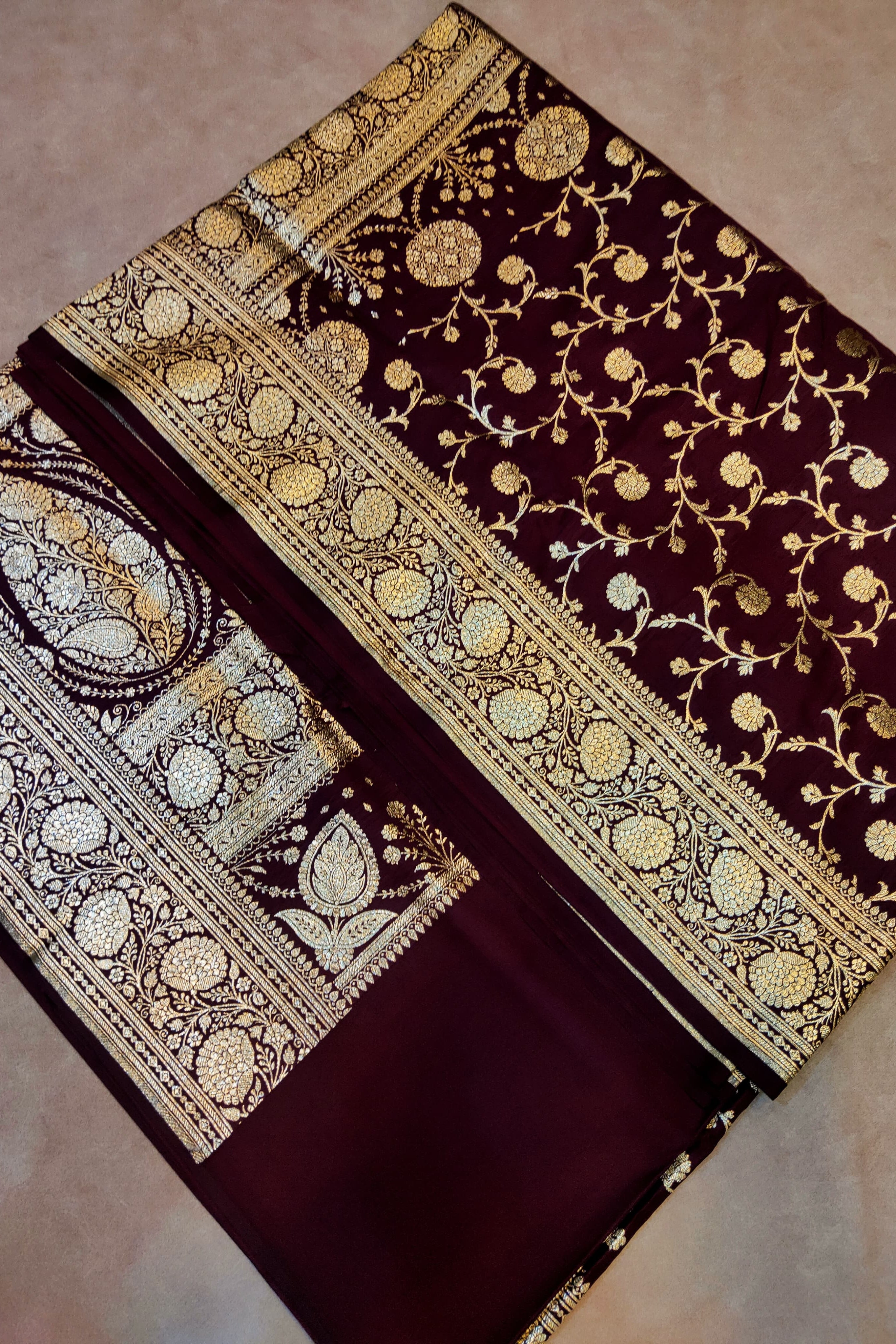 Brown saree with gold and white floral patterns on a beige background