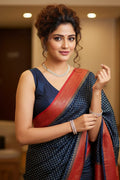 Woman in a navy blue saree with a red border indoors