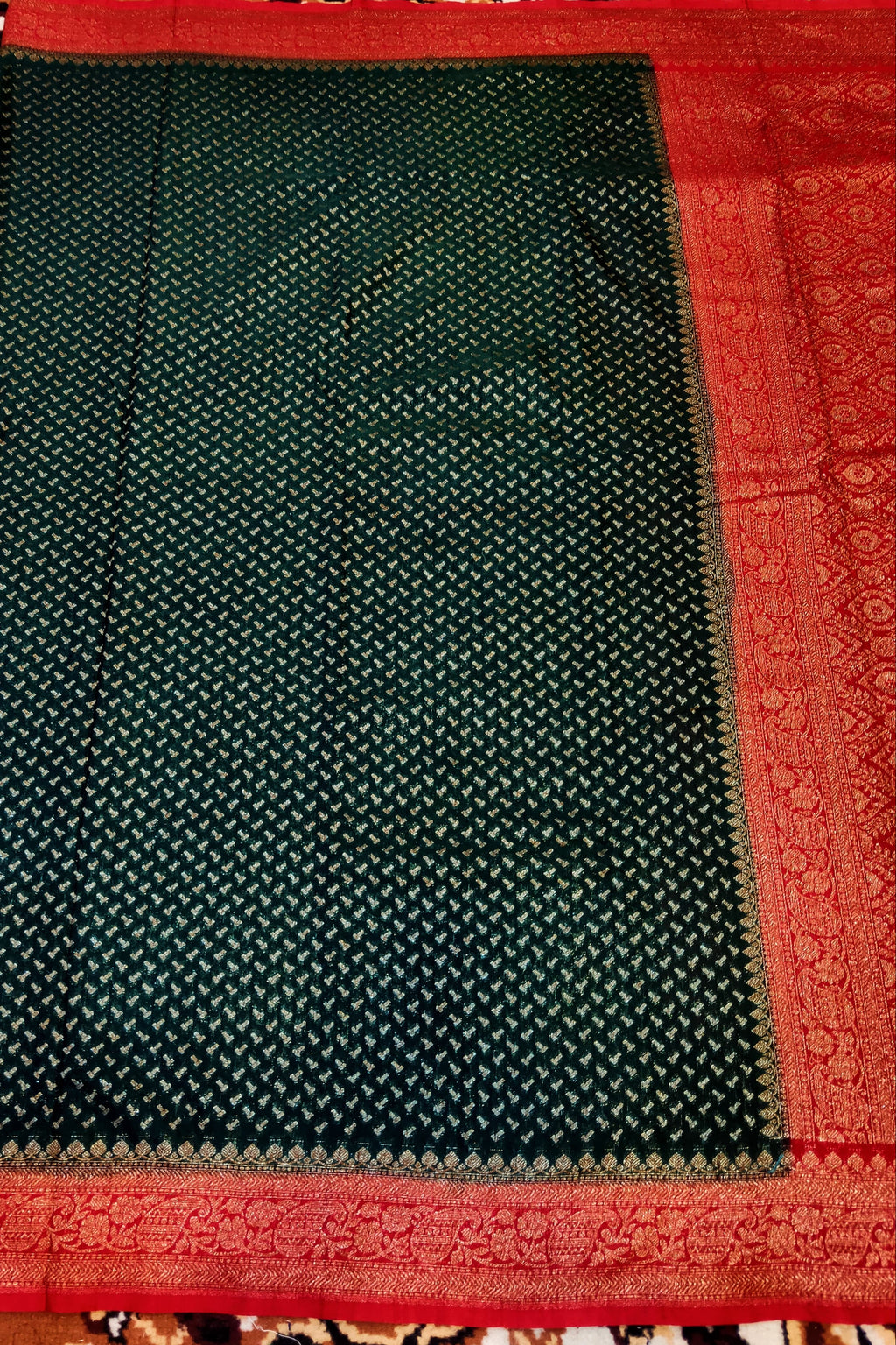 Dark green saree with red border on a patterned fabric background