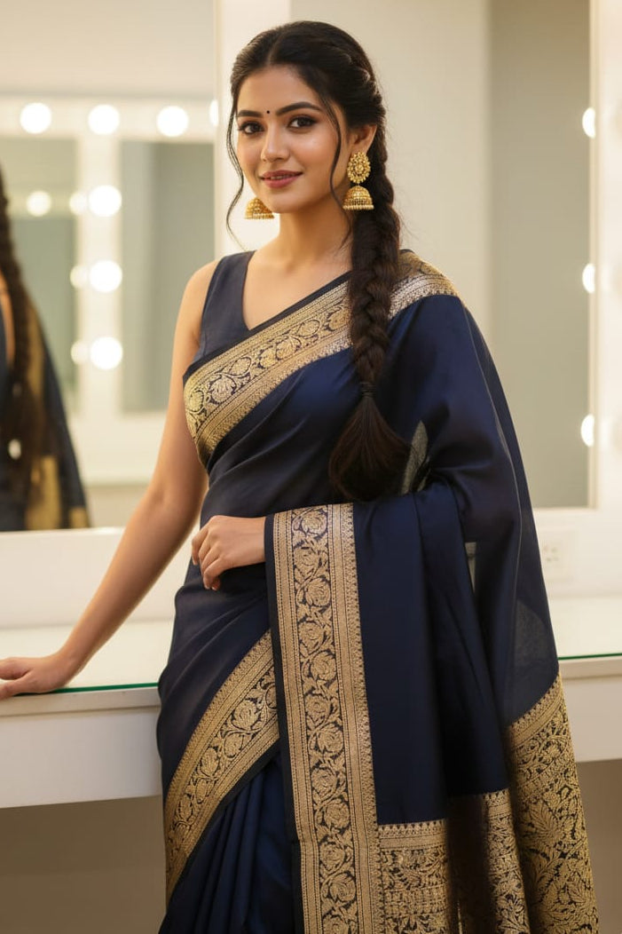Woman in a navy blue saree with gold patterns standing in front of a mirror.