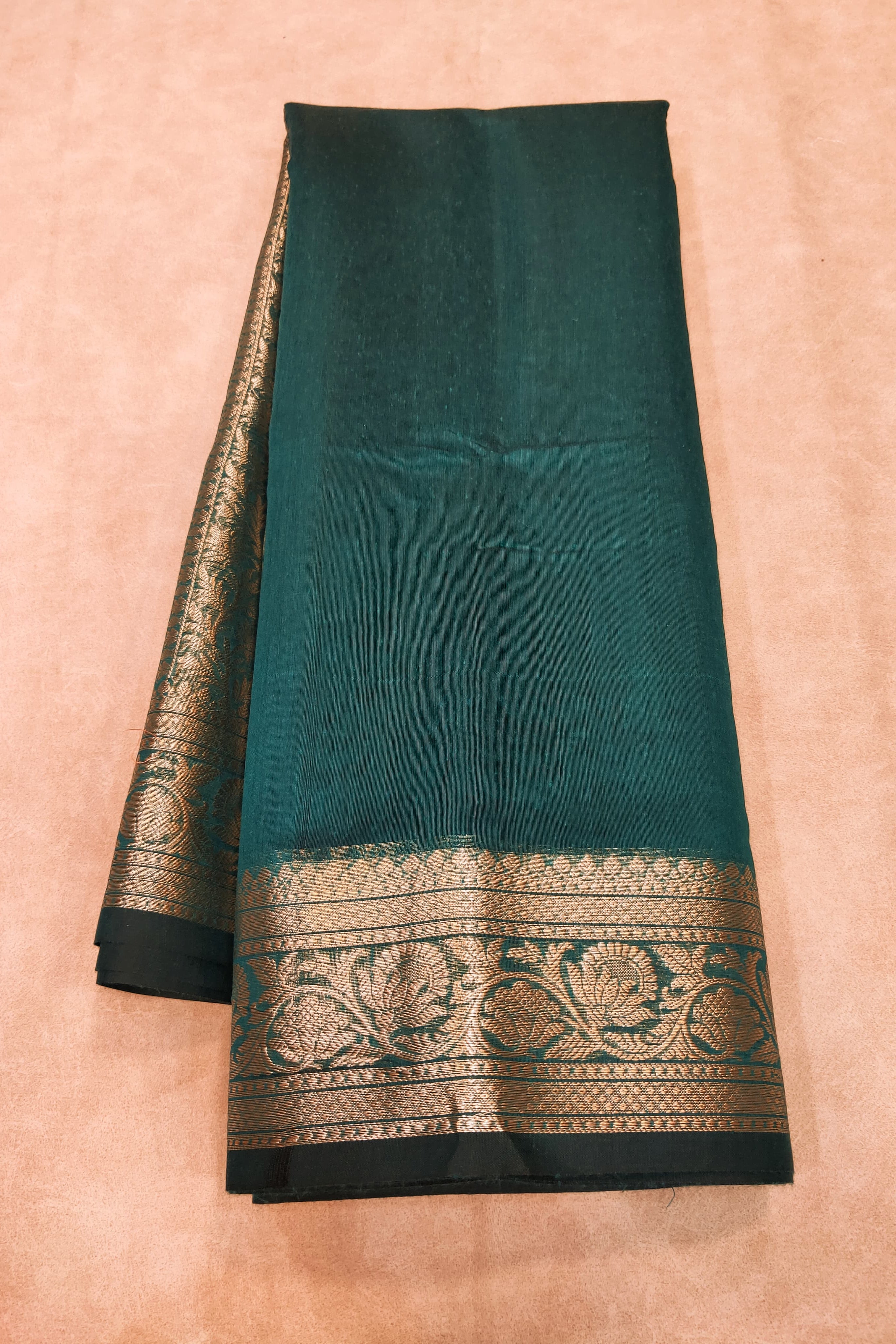 Teal saree with black and gold border on a beige background