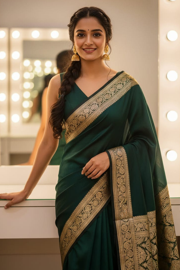 Woman in a green saree with gold border standing in front of a mirror with lights.