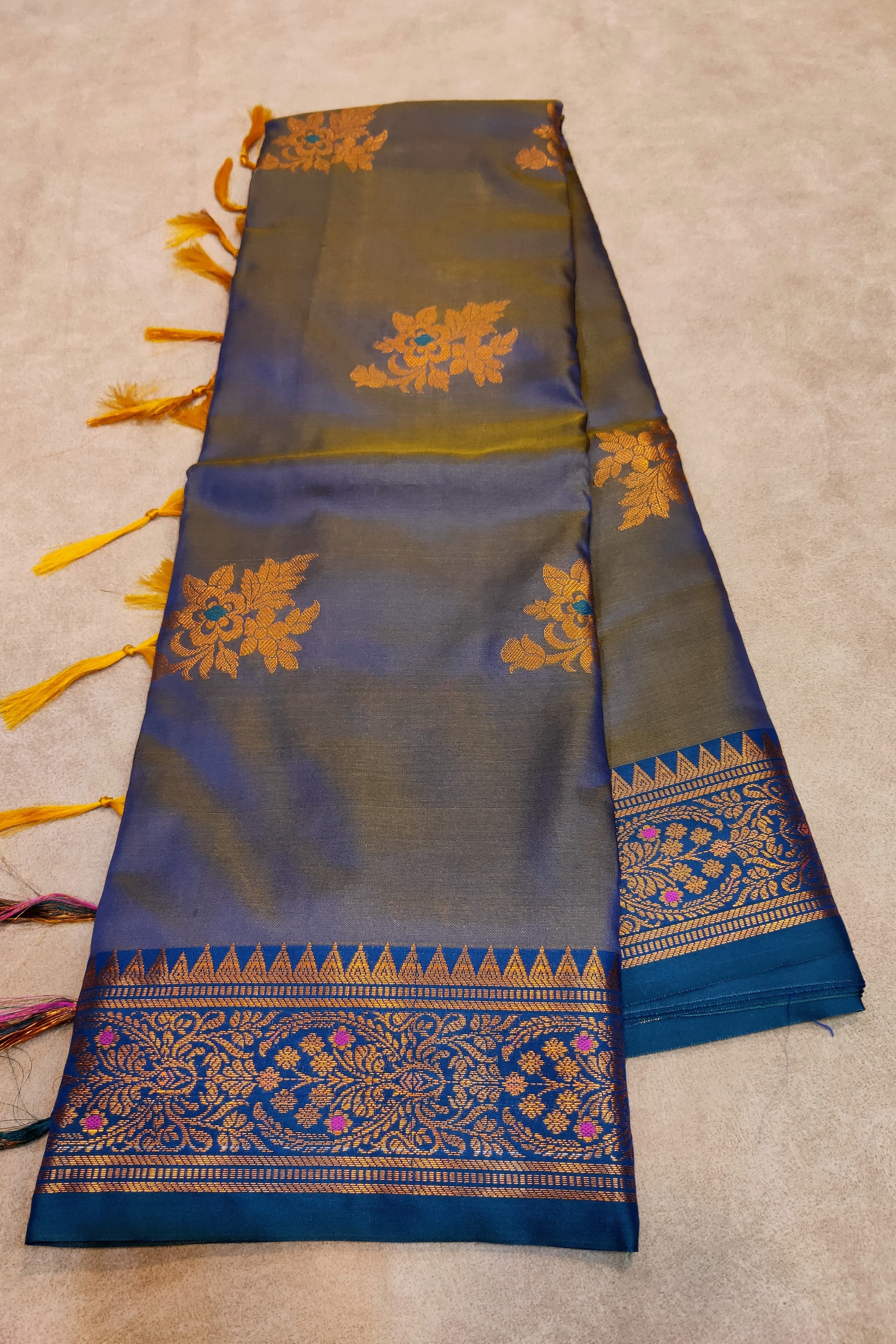 Blue and green saree with gold embroidery on a beige background
