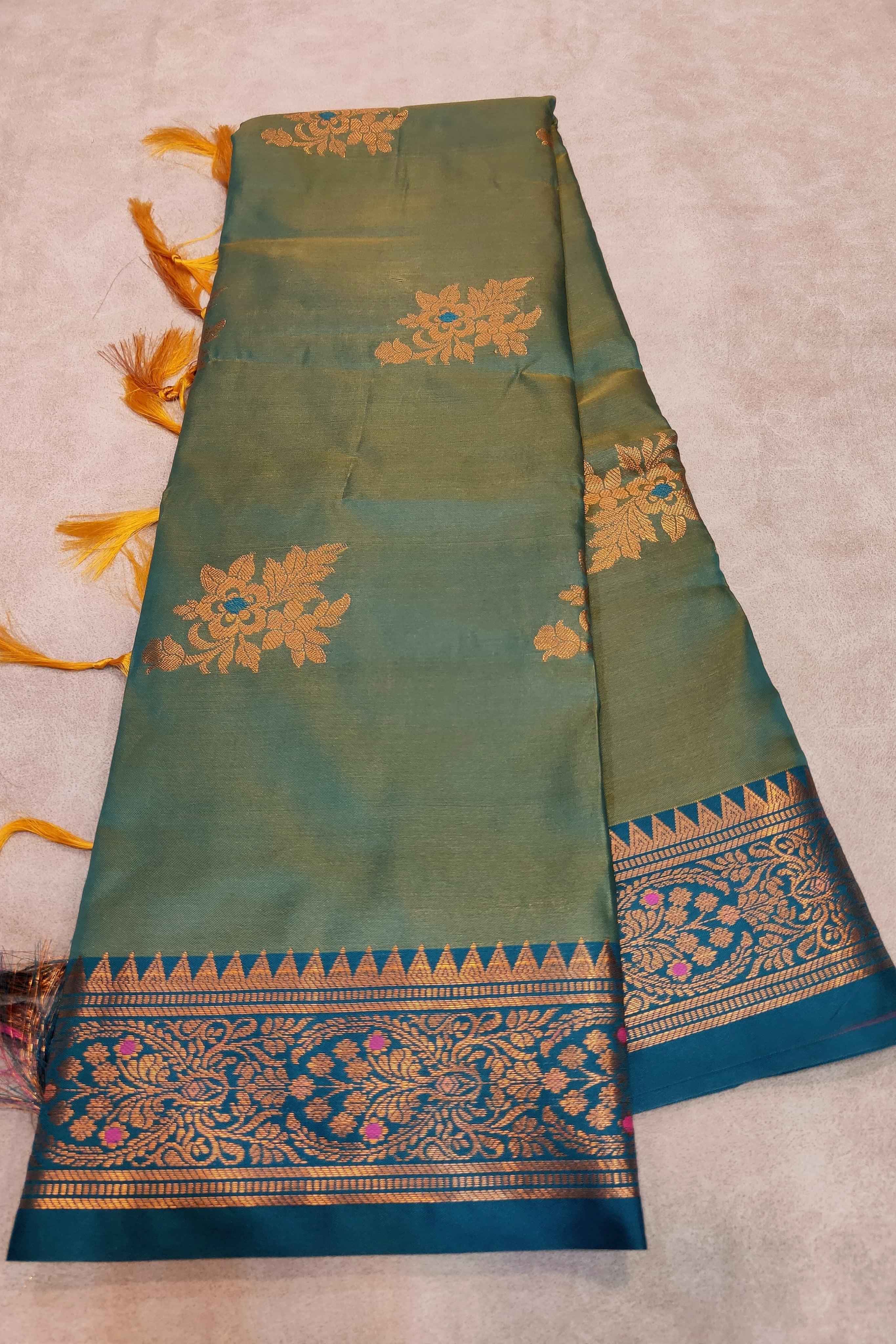 Green saree with gold and blue border on a beige background