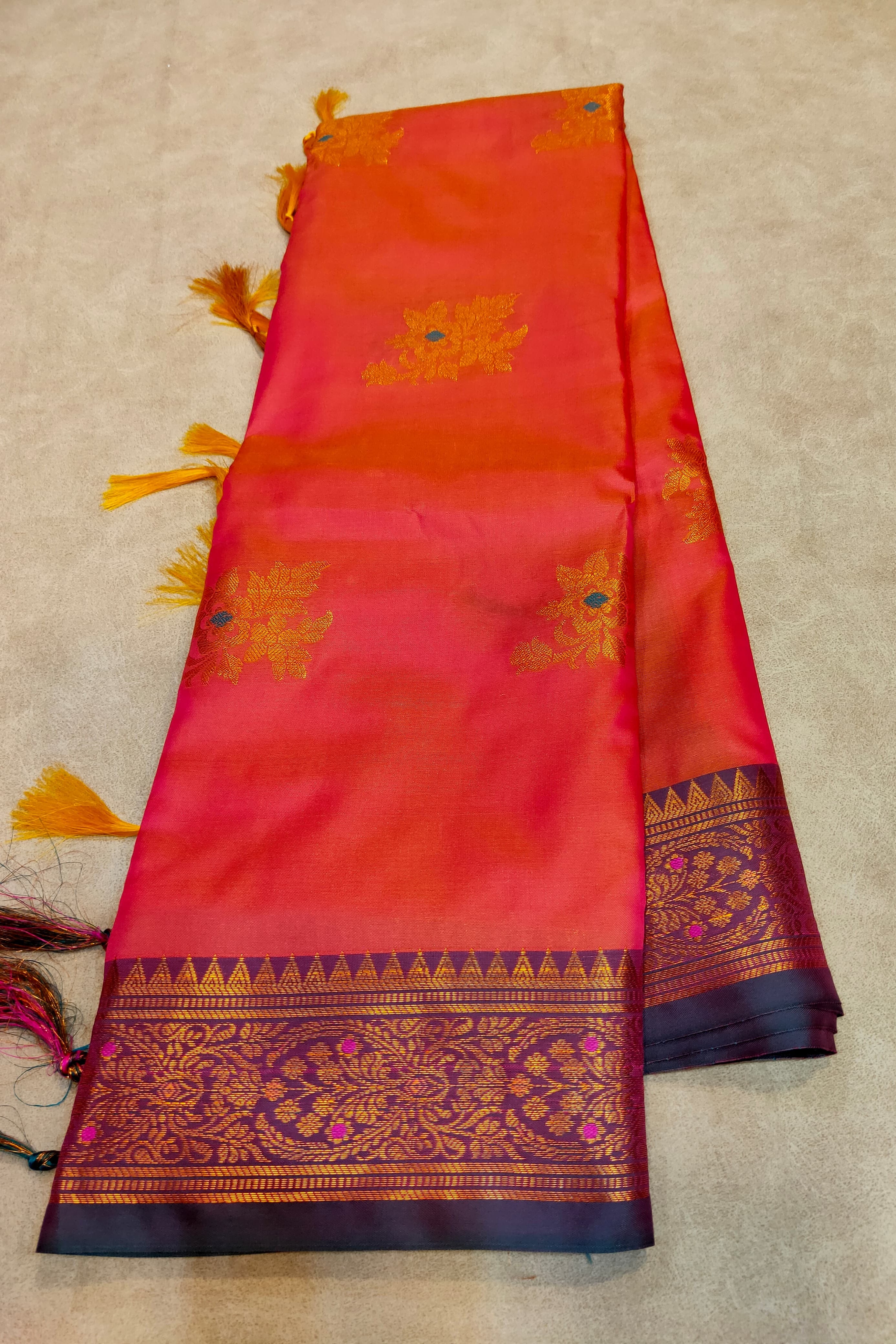 Red and orange saree with gold and blue patterns on a beige background