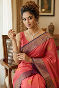 Woman in a pink saree with intricate designs sitting indoors.